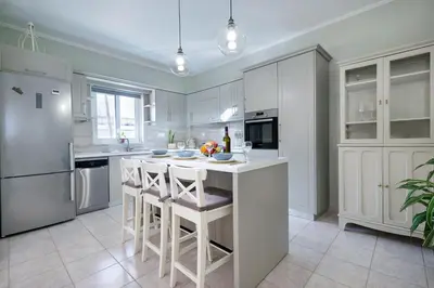 a kitchen with white cabinets and a white island with bar stools at Gigis Apartment in Chania Town