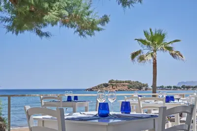 a table with white chairs and a palm tree and water at Atlantica Kalliston Resort - Adults Only in Stalos