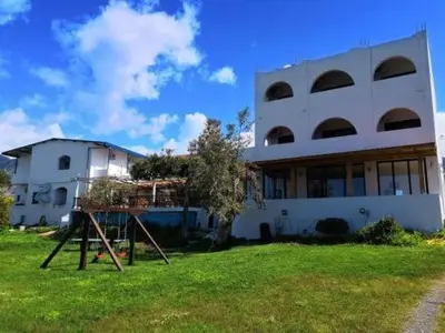 a large white building with a tree in front of it at Babis & Popi Rooms and Studios in Frangokastello