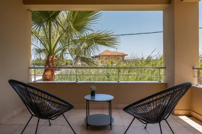 two chairs and a table on a balcony with a palm tree at Villa Per Mare in Maleme