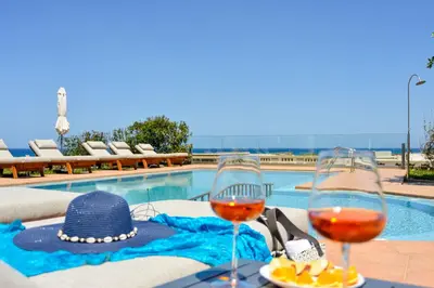 a table with two glasses of wine next to a swimming pool at Panthea Luxury Living in Kolymvari