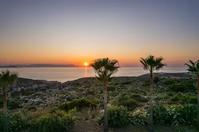 a sunset over the ocean with palm trees at Natura Hill Villa III Sunset View in Kounoupidhianá