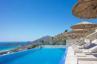 a pool with chairs and umbrellas and the ocean at Flower Village in Chania Town