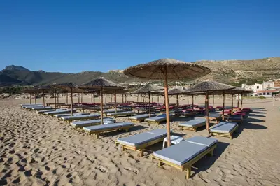 a row of umbrellas and lounge chairs on a beach at En Plo Beachfront Rooms in Falasarna