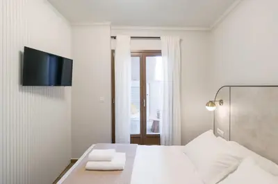 a white bedroom with a bed and a tv on the wall at In Heart of Old Town Saint Rocco's Chic Apt in Chania Town