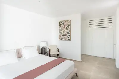a white bedroom with a bed and a chair at Villa Inati in Nípos
