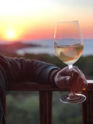 a person holding a glass of wine with the sunset in the background at Glykeria Hotel in Elafonisi