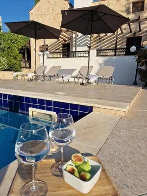a table with wine glasses and a bowl of fruit next to a pool at Villa Penelope Luxury Retreat with Pool & Timeless Charm in Douliana