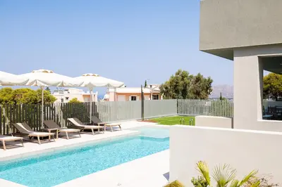 a swimming pool with chairs and umbrellas next to a house at Heliades Residence in Kounoupidhianá