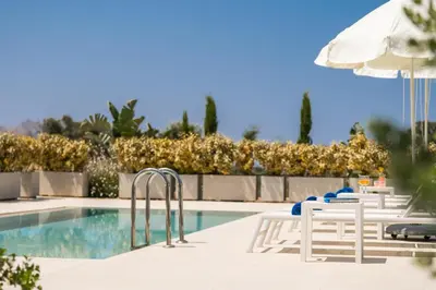 a row of chairs and an umbrella next to a swimming pool at Dioni by PosarelliVillas in Kounoupidhianá