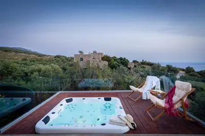 a hot tub on a deck with a castle in the background at Blue Pearl Villa in AmigdhalokeFálion