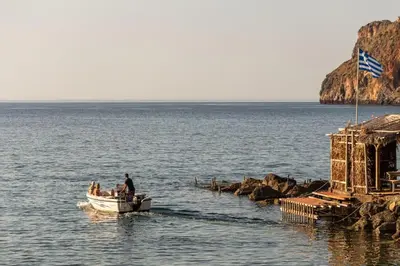 a man in a small boat in the water at Celeste Junior Suite on the Beach in Agia Marina Nea Kydonias