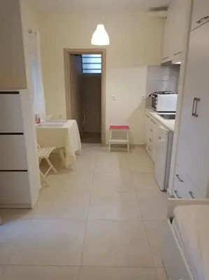 a white kitchen with a table and a pink stool at happy travelers studio free parking in Chania Town