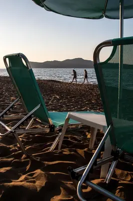 two people walking on a beach with two lawn chairs at Papidakis Studios in Agia Marina Nea Kydonias