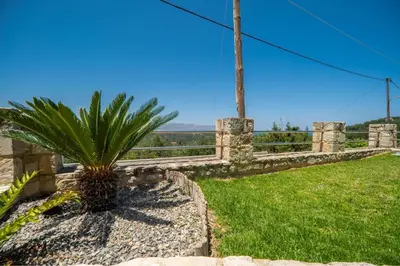 a palm tree sitting in the grass next to a fence at Villa Nimertis in Xirokámbion