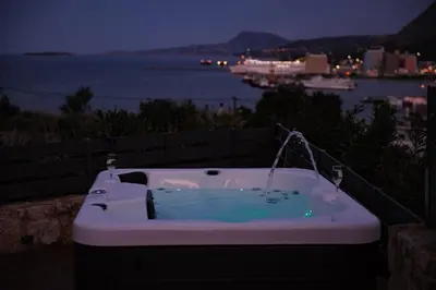 a bath tub with a view of the ocean at night at Thearia villa I - seaview , private heated pool & jacuzzi in Souda