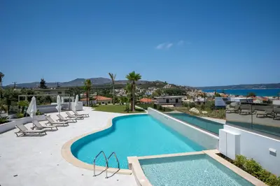 a large swimming pool with lounge chairs and the ocean at AmphiMatrion Luxury Residence in Kalyves