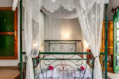 a canopy bed with white curtains and pink flowers on it at IFIGENIA TRAD.ROOMS IN OLDTOWN BY.MARIOS in Chania Town