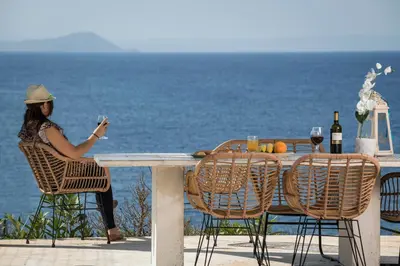 a woman sitting at a table with a glass of wine at Seafront Villa Shore, Sea & Sun Villas in Chorafakia