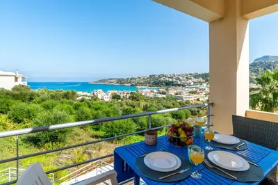a table with wine glasses and a bowl of fruit on a balcony at Almyrida Bay View House II BY APOKORONAS-VILLAS in Almirida