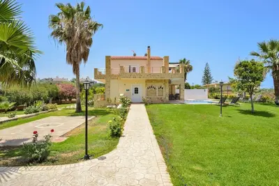 a large yellow house with palm trees and a driveway at Elma's Villa: A peaceful, family-friendly place in Daratso