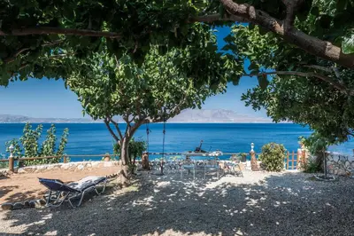 a beach with chairs and a tree and the ocean at 2 annexed apartments -Private place to swim-large terrace- Unlimited view in Ravdhoúkha