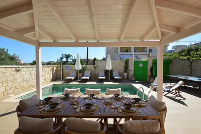 a dining table and chairs under a pavilion next to a pool at Villa Ithaca in Varípetron