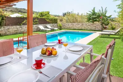 a table with a bowl of fruit on it next to a swimming pool at Villa Lemonia Platanias in Plataniás
