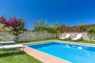 a swimming pool with two lawn chairs and a fence at Villa Mandarin Platanias in Plataniás
