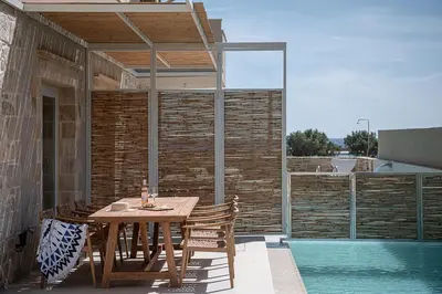 a wooden table and chairs on a patio with a pool at Pietra Di Sabbia Villas in Palaiochóra