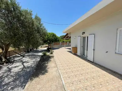 a white house with a brick walkway and trees at Olivia House -BY APOKORNAS VILLAS in Káïna