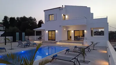 a white house with a swimming pool in front of it at Montis villa sea view heated pool in Daratso