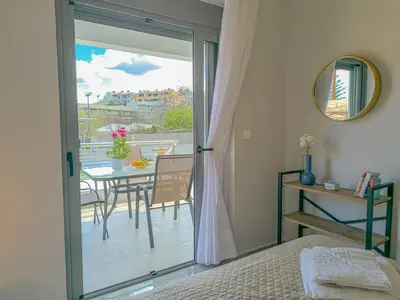 a bedroom with a door open to a balcony with a table at Newly Built House Steps from the Beach: Everything Within Walking Distance - Enjoy a Car-Free Stay in Agia Marina Nea Kydonias