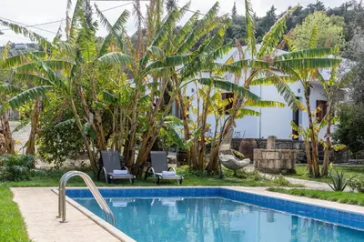 a pool with two chairs and a house with trees at Klapas by PosarelliVillas in Chania Town