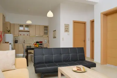 a living room with a black couch and a kitchen at AVRA COZY APARTMENT Agioi Apostoloi Chania in Daratso