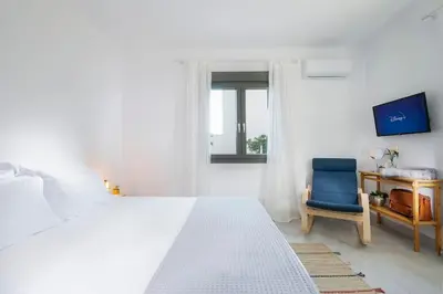 a white bedroom with a bed and a blue chair at Olive Apt - Akrotiri in Kounoupidhianá
