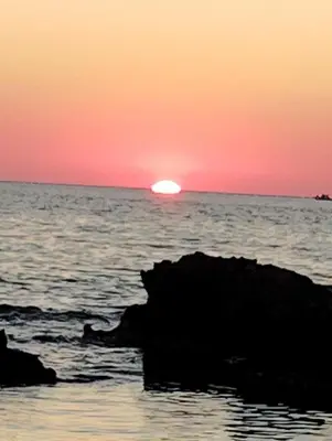 a sunset over the ocean with a rock in the water at Levendi's House in Kissamos