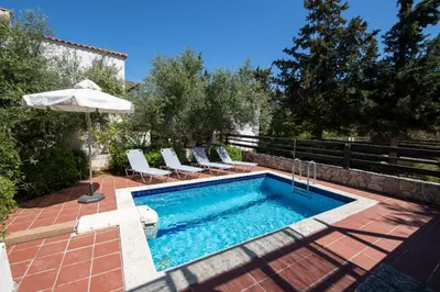 a pool with chairs and an umbrella on a patio at Villa Olivia in Chania Town