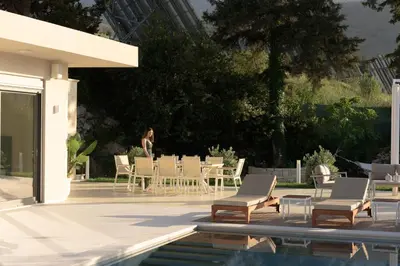a woman standing on a patio with chairs and a pool at Reflection Villa, Heated Pool & Absolute Seclusion, By ThinkVilla in Chania Town