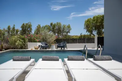 a swimming pool with white tables and chairs next to it at Mons Villa in Kalathas