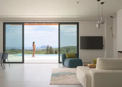 a living room with a woman looking out the sliding glass door at Blue Zone Villa, a SeaView Sanctuary with Pool, By ThinkVilla in Chania Town