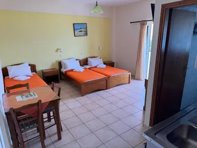 a room with two beds and a table and a kitchen at Michalis Studios & Aparntments in Palaiochóra