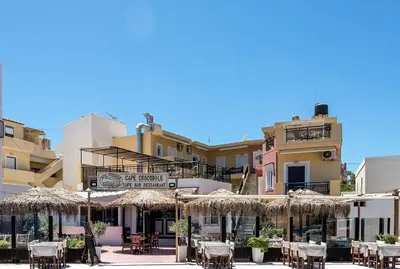 a patio with tables and umbrellas in front of buildings at Harbour Studios And Apartments in Palaiochóra