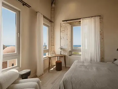 a bedroom with a bed and a desk and two windows at Aisha Hotel in Chania Town