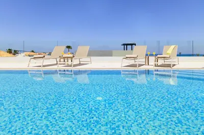 a swimming pool with chairs and a table and the water at Beach Sand Villas - Beachfront Roof Pool Seaviews in Pírgos Psilonérou