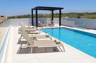 a pool with chaise lounge chairs and a swimming pool at Beach Sand Villas - Beachfront Roof Pool Seaviews in Pírgos Psilonérou