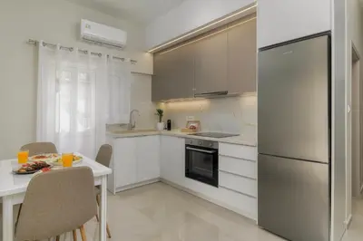 a white kitchen with a table and a refrigerator at SugarDustApt Elegant Retreat 150m from the Sea in Chania Town