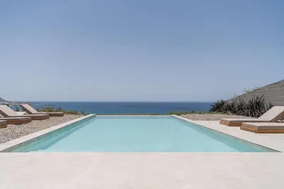 a swimming pool with chairs and the ocean in the background at Alba Cave Villas in Chania Town