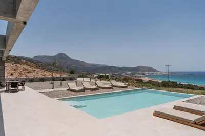 a swimming pool with lounge chairs and the ocean at Alba Cave Villas in Chania Town