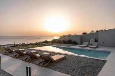 a swimming pool with lounge chairs and the ocean at Alba Cave Villas in Chania Town